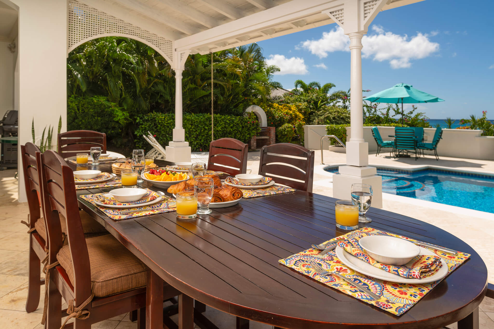 Outdoor dining area with a long wooden table laid for six people with croissants and a fruit platter