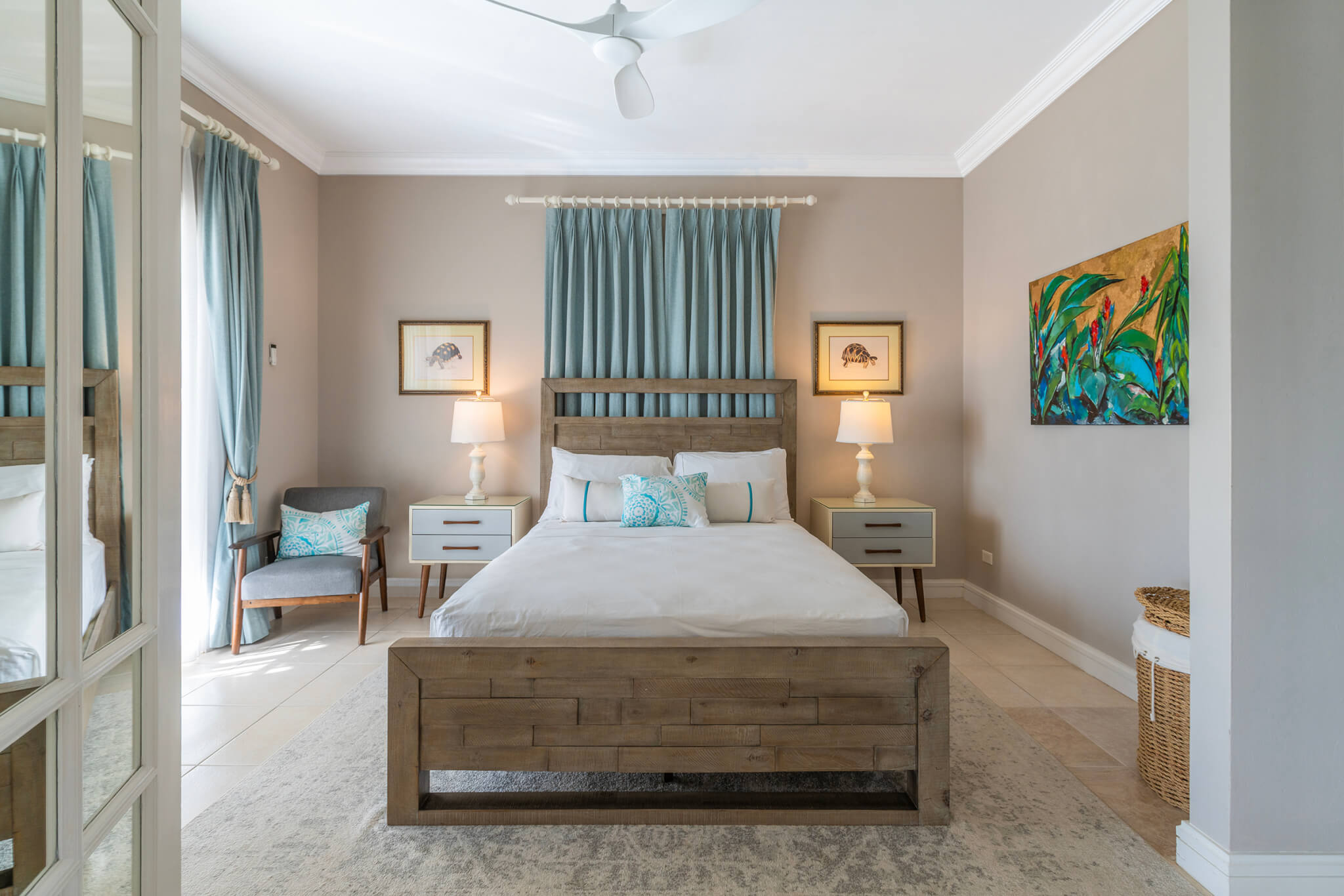 Bedroom with a king size bed and a blue curtain behind the bed with a colourful painting on one wall and a balcony to the other side